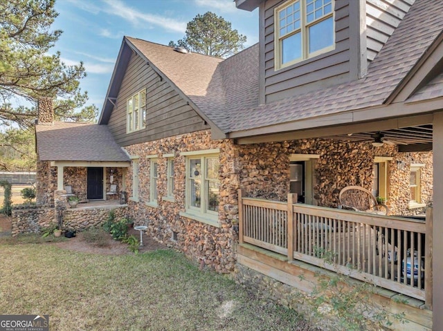 exterior space with a shingled roof, stone siding, a yard, and a ceiling fan