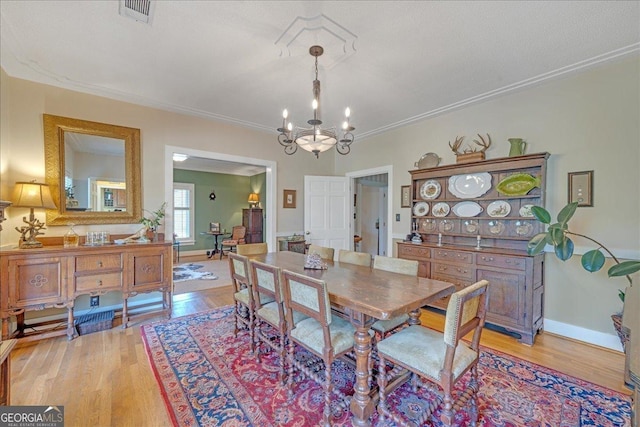 dining area with crown molding, visible vents, baseboards, light wood-type flooring, and an inviting chandelier