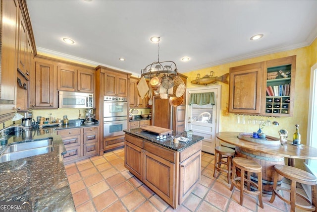 kitchen with crown molding, stainless steel appliances, brown cabinetry, a sink, and a kitchen island