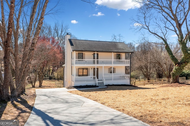 view of front of home with a shingled roof, a balcony, a chimney, covered porch, and fence