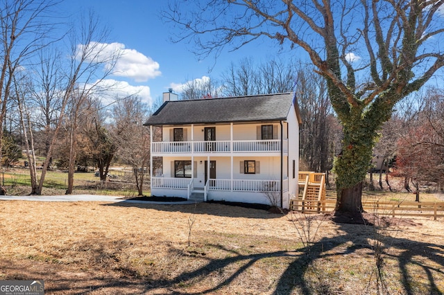 view of front facade featuring a balcony, covered porch, a chimney, and roof with shingles