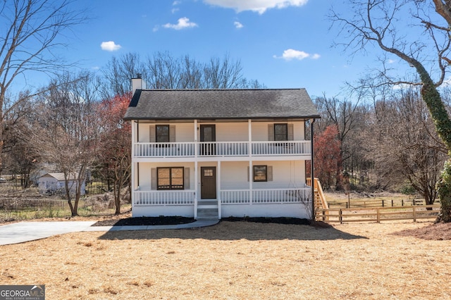 view of front of house with a balcony, covered porch, fence, roof with shingles, and a chimney