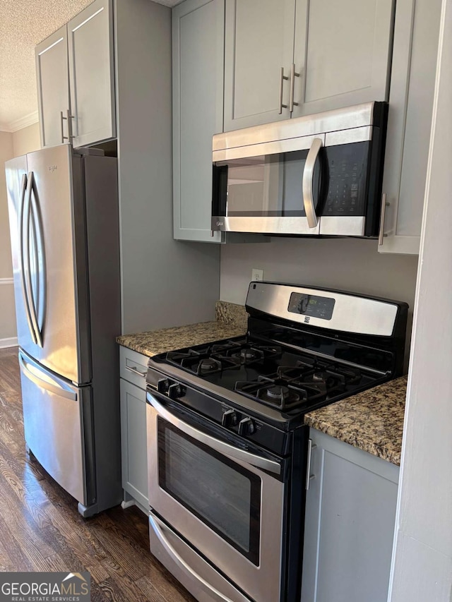 kitchen featuring dark wood finished floors, gray cabinets, appliances with stainless steel finishes, stone countertops, and a textured ceiling