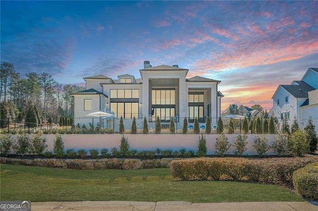 back of property at dusk with a fenced front yard and a yard