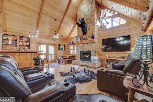 living area featuring a stone fireplace, wooden ceiling, wood walls, wood finished floors, and a ceiling fan