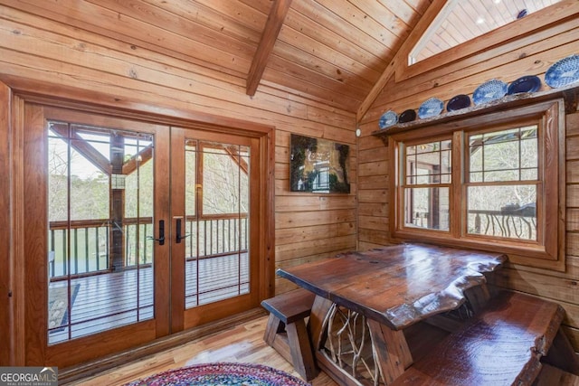 dining room with wooden ceiling, wooden walls, light wood-style floors, vaulted ceiling, and french doors