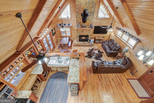 living room with beam ceiling, ceiling fan, a stone fireplace, high vaulted ceiling, and wooden ceiling