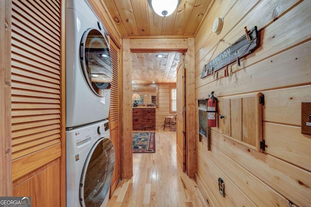 laundry area with wooden ceiling, light wood-style flooring, wooden walls, laundry area, and stacked washing maching and dryer