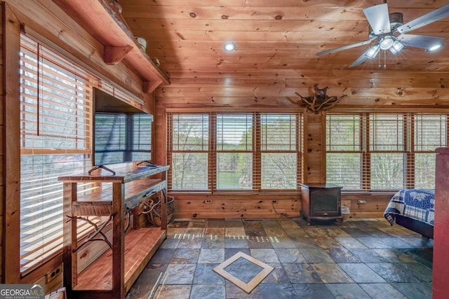 sunroom / solarium with wood ceiling, a wood stove, and a ceiling fan