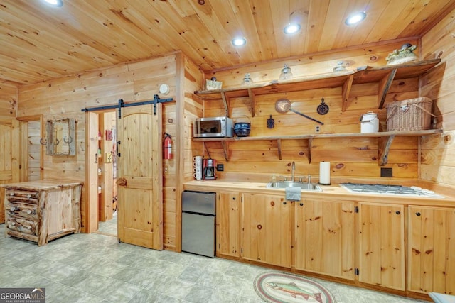 kitchen featuring a barn door, appliances with stainless steel finishes, wood ceiling, a sink, and wooden walls