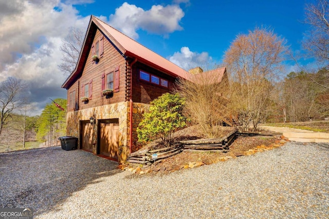 view of property exterior with gravel driveway, stone siding, an attached garage, and metal roof