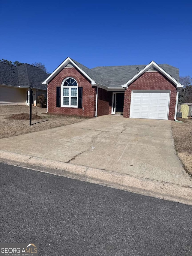 ranch-style home with an attached garage, roof with shingles, concrete driveway, and brick siding