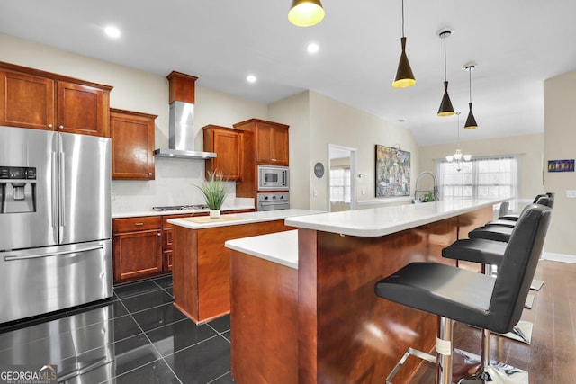 kitchen with wall chimney exhaust hood, a center island with sink, stainless steel appliances, and light countertops