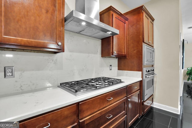 kitchen featuring dark tile patterned flooring, light countertops, appliances with stainless steel finishes, decorative backsplash, and wall chimney exhaust hood