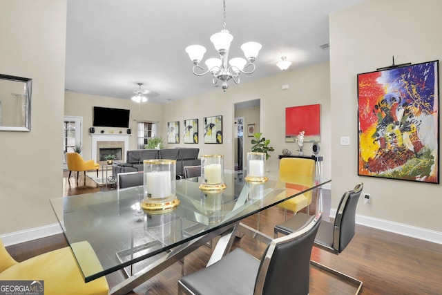 dining space featuring ceiling fan with notable chandelier, a tile fireplace, baseboards, and wood finished floors