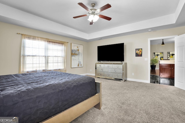 carpeted bedroom with ceiling fan, a tray ceiling, ensuite bath, and baseboards