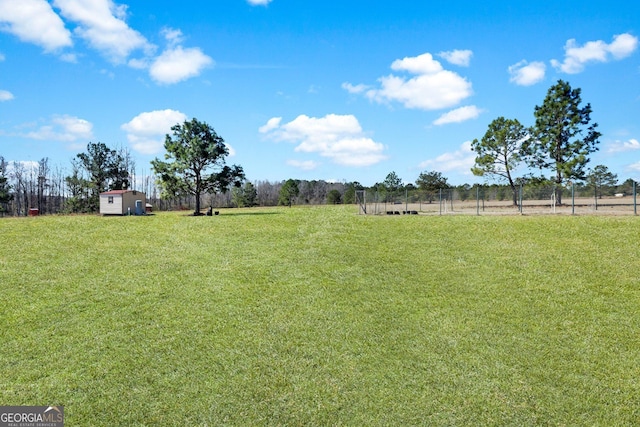 view of yard featuring a storage unit, a rural view, fence, and an outdoor structure