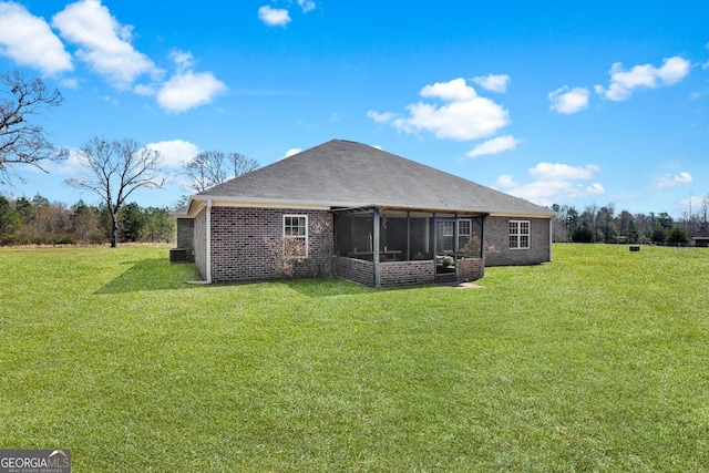 back of house featuring a shingled roof, a sunroom, brick siding, and a yard