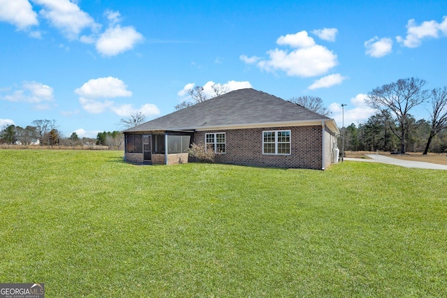 rear view of house with a shingled roof, a sunroom, brick siding, and a lawn