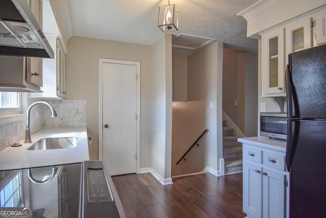 kitchen featuring dark wood-type flooring, freestanding refrigerator, light countertops, under cabinet range hood, and a sink