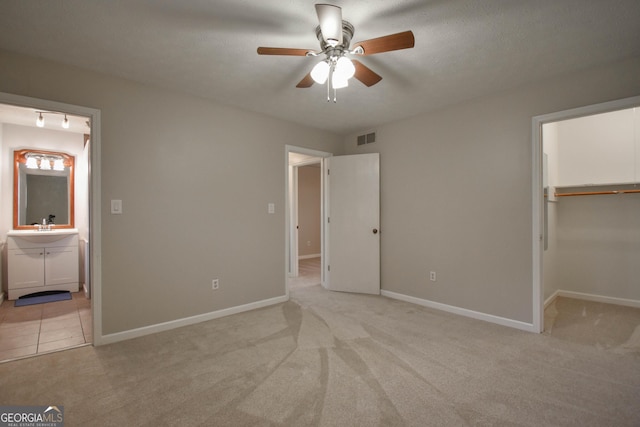 unfurnished bedroom featuring a spacious closet, visible vents, ensuite bathroom, and light colored carpet