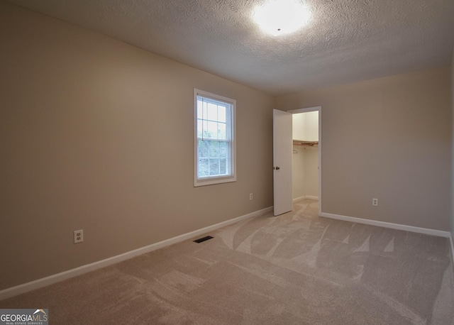 unfurnished bedroom with visible vents, light colored carpet, a textured ceiling, and baseboards