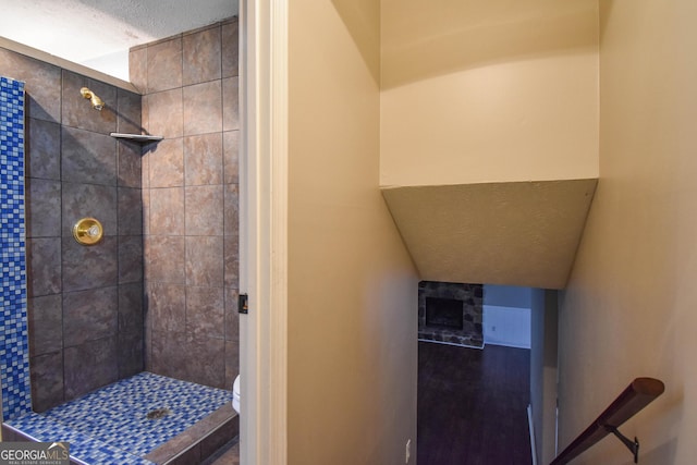 bathroom with a textured ceiling, a tile shower, and toilet