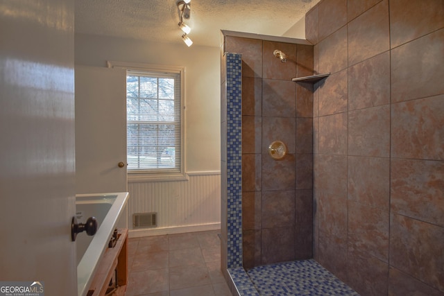 full bath featuring wainscoting, visible vents, a textured ceiling, and tiled shower