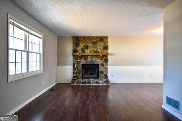 unfurnished living room featuring visible vents, wainscoting, hardwood / wood-style floors, a textured ceiling, and a fireplace