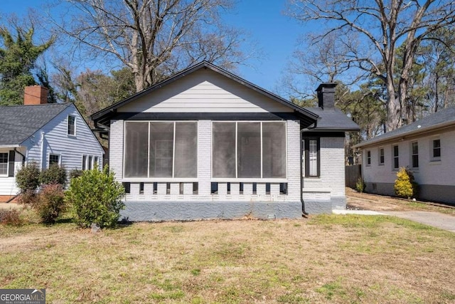 exterior space with a sunroom, a chimney, a lawn, and brick siding