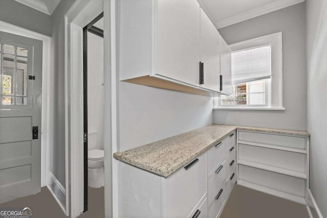 interior space with light stone countertops, ornamental molding, and white cabinets