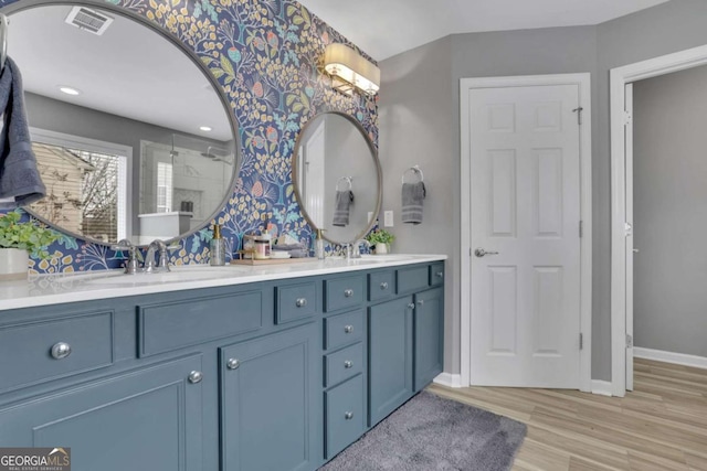 full bathroom with wood finished floors, a sink, visible vents, a shower, and double vanity