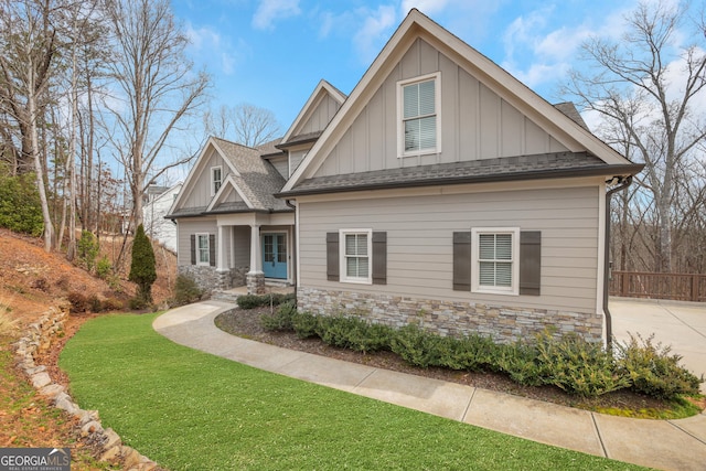 craftsman inspired home featuring a shingled roof, fence, stone siding, a front lawn, and board and batten siding