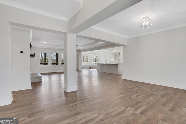 unfurnished living room featuring a chandelier, ornamental molding, wood finished floors, and baseboards