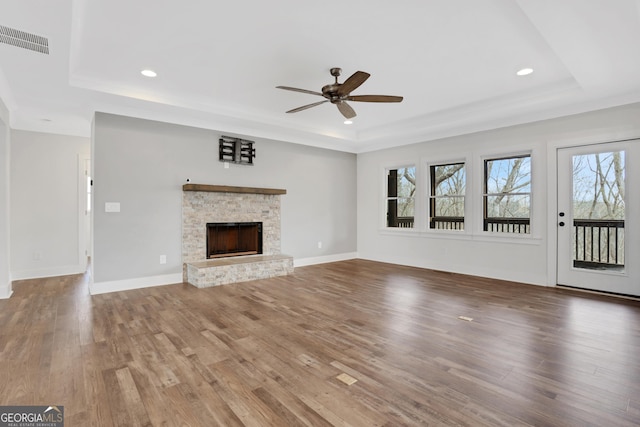 unfurnished living room with a fireplace, visible vents, a raised ceiling, and wood finished floors