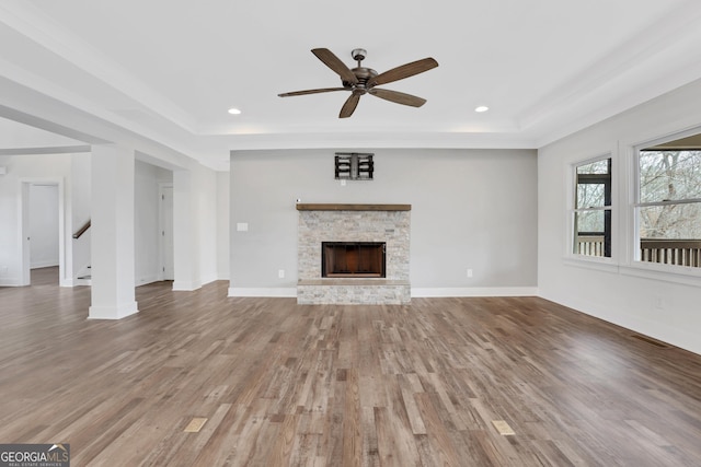 unfurnished living room with light wood-type flooring, a tray ceiling, a fireplace, and baseboards