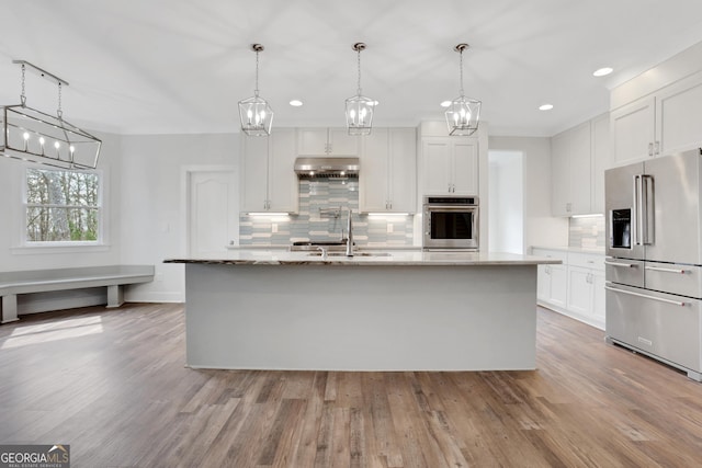 kitchen featuring white cabinets, wood finished floors, stainless steel appliances, under cabinet range hood, and a sink