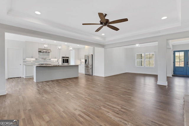 unfurnished living room featuring a tray ceiling, recessed lighting, a sink, wood finished floors, and baseboards