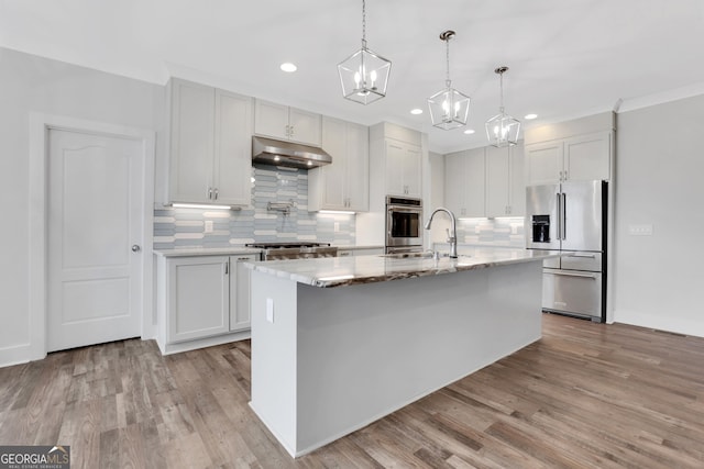 kitchen featuring appliances with stainless steel finishes, a sink, light wood-type flooring, under cabinet range hood, and backsplash