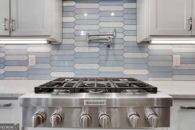 room details featuring white cabinetry, stainless steel gas stovetop, light stone counters, and backsplash