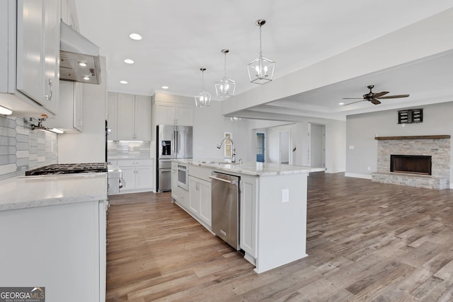 kitchen featuring light wood finished floors, open floor plan, stainless steel appliances, a sink, and exhaust hood