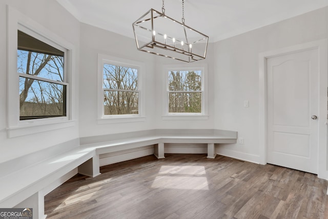 unfurnished dining area with a chandelier, ornamental molding, baseboards, and wood finished floors