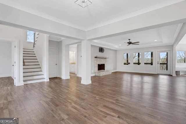 unfurnished living room featuring a fireplace with raised hearth, wood finished floors, baseboards, stairs, and a raised ceiling