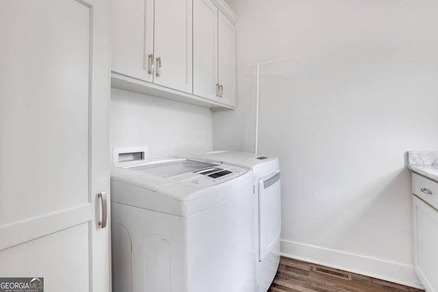 washroom with cabinet space, baseboards, visible vents, dark wood-style flooring, and washing machine and clothes dryer