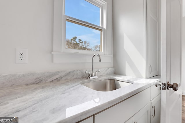 kitchen with light stone countertops, white cabinets, and a sink