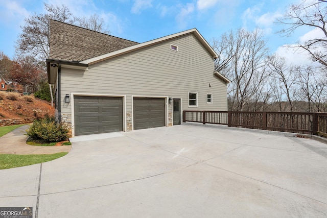 view of home's exterior featuring a garage, driveway, a shingled roof, and stone siding