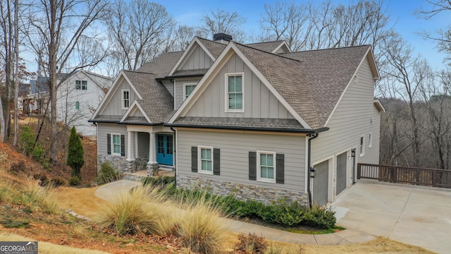 craftsman house featuring a shingled roof, stone siding, concrete driveway, board and batten siding, and a chimney