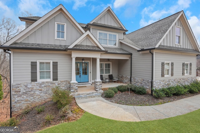 craftsman inspired home with board and batten siding, stone siding, roof with shingles, and french doors