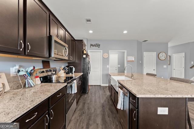 kitchen featuring a kitchen island with sink, stainless steel appliances, a sink, light stone countertops, and dark wood finished floors