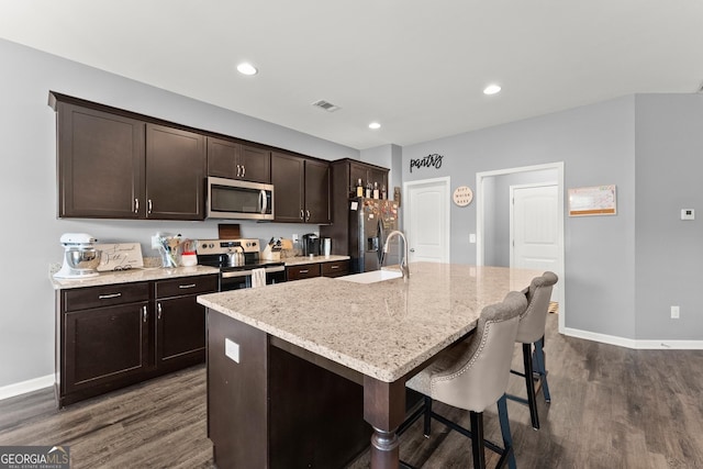 kitchen with visible vents, dark wood-style floors, a kitchen island with sink, stainless steel appliances, and a sink